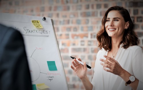 A smiling woman holding a pen next to a flipchart that has "strategies" written on it.
